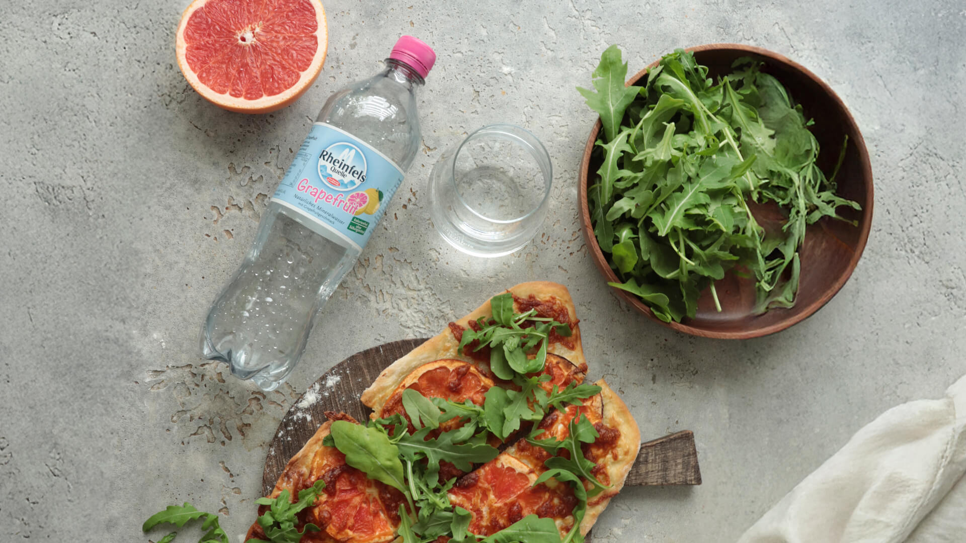 Flammkuchen mit Grapefruit und Rucola daneben liegt eine Flasche Rheinfels Quelle Grapefruit