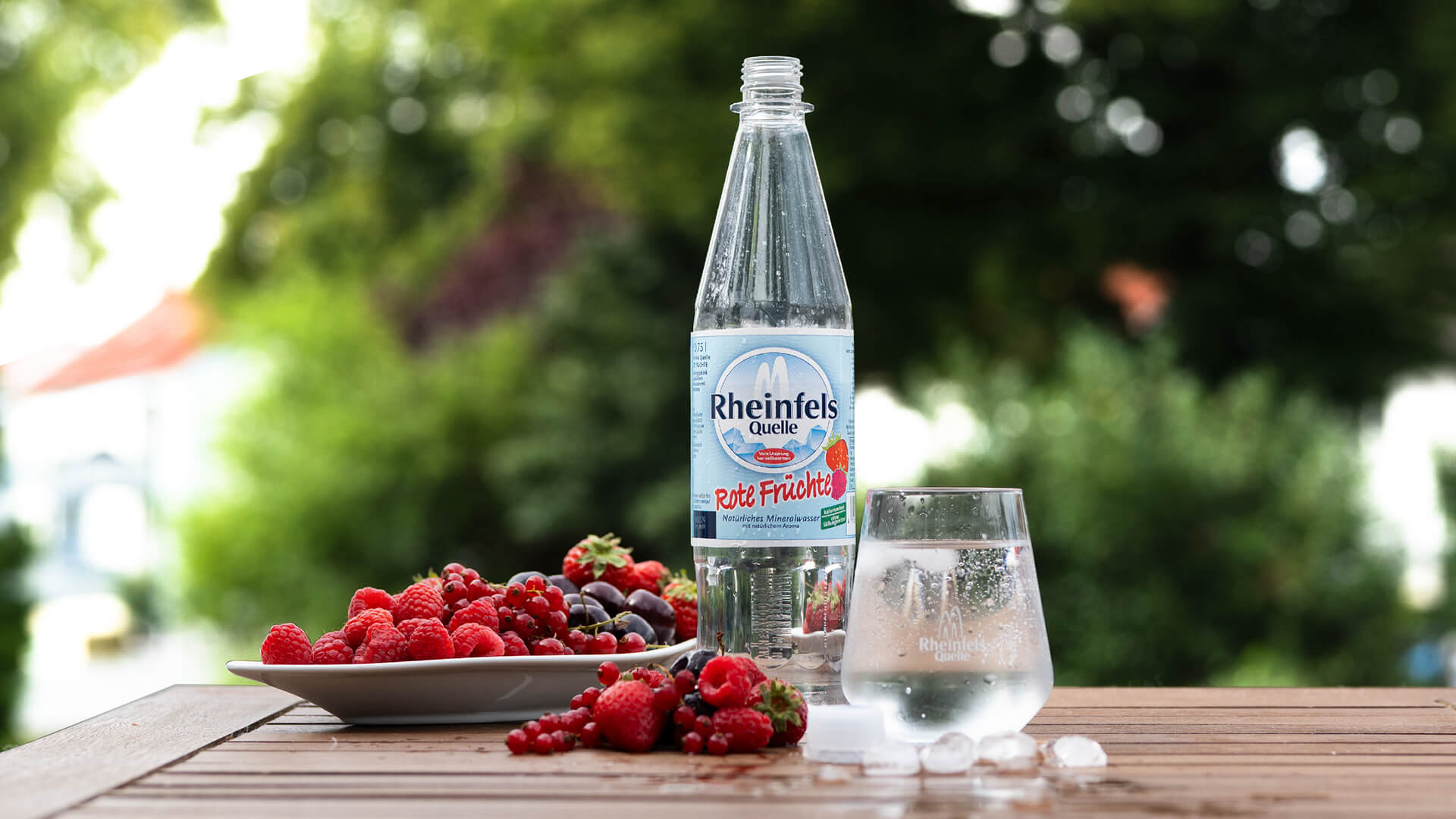 Rheinfels Rote Früchte Flasche auf dem Gartentisch, daneben ein Teller mit Beeren