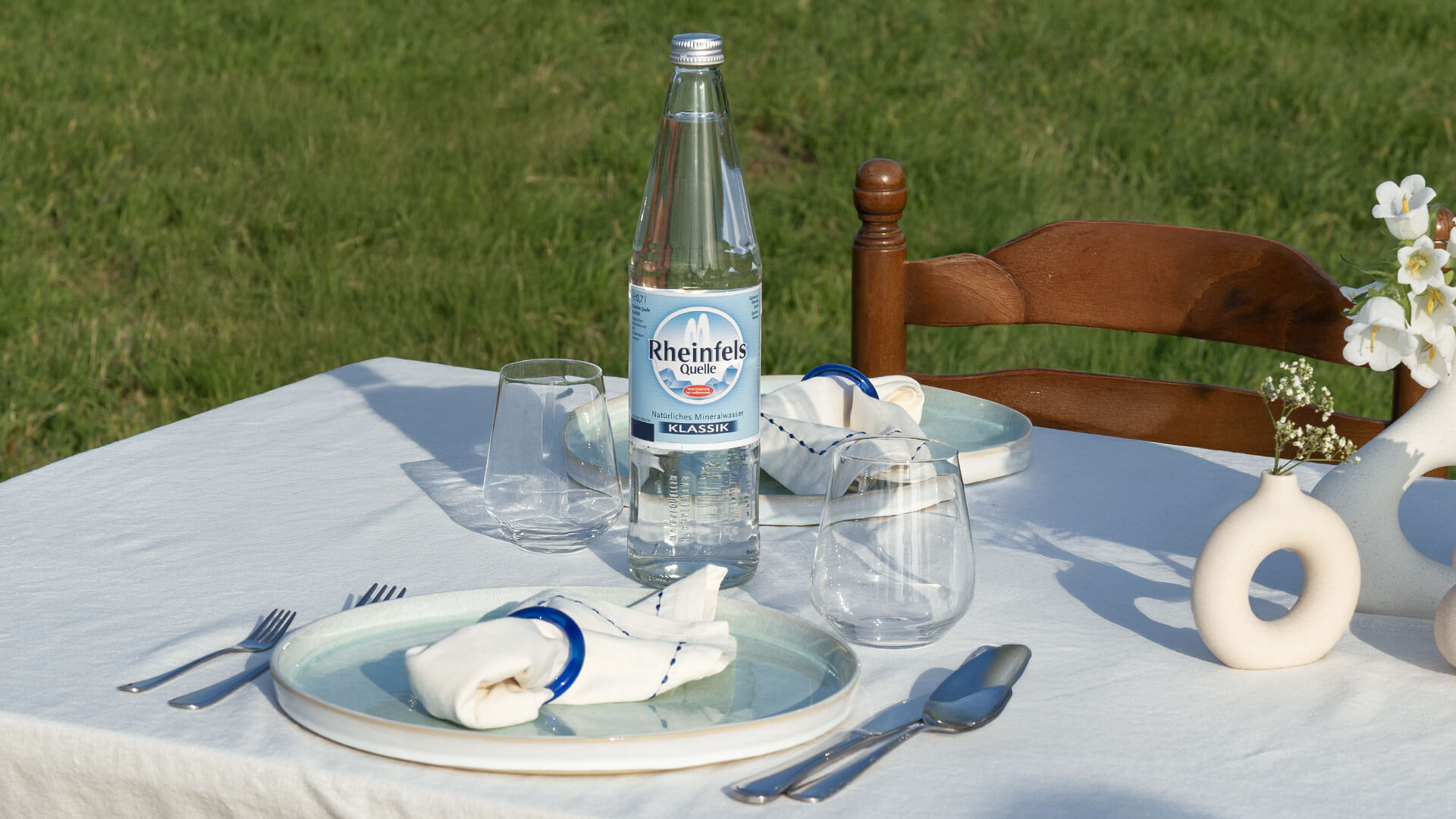 Rheinfels Quelle Klassik in der Glasflasche steht auf einem gedeckten Tisch.
